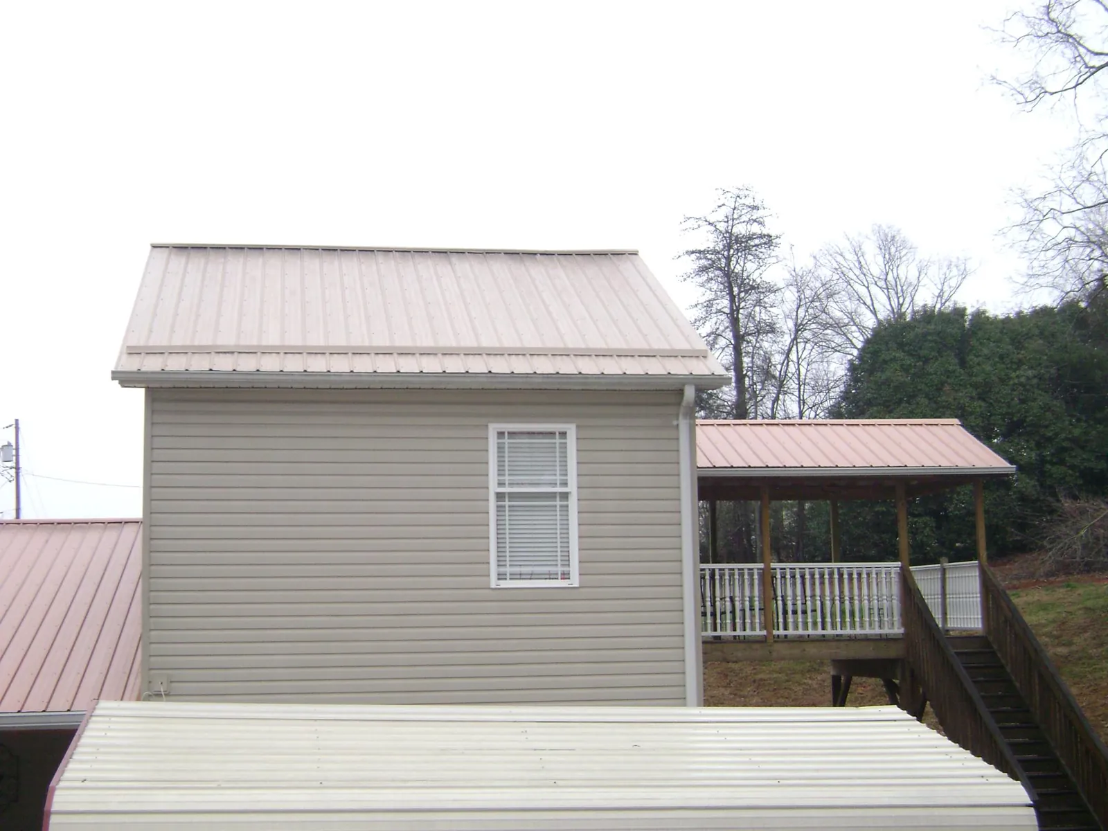 Tan metal roofs on a two story addition and attached porch, from a Roof Replacement job in Meriden